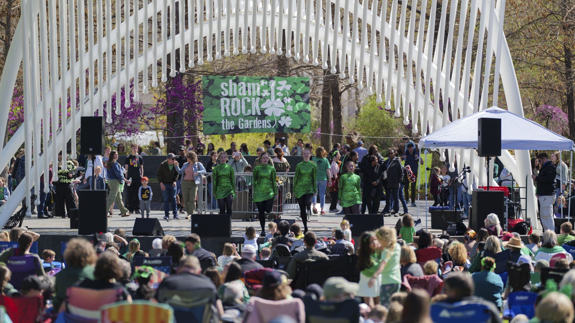 Traditional Irish dancers perform in sequined green dresses on the outdoor stage at Myriad Gardens while a large crowd watches.