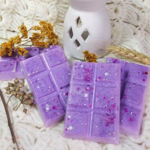 Purple wax molds sit on a beige blanket with a white wax warmer and dried flowers.