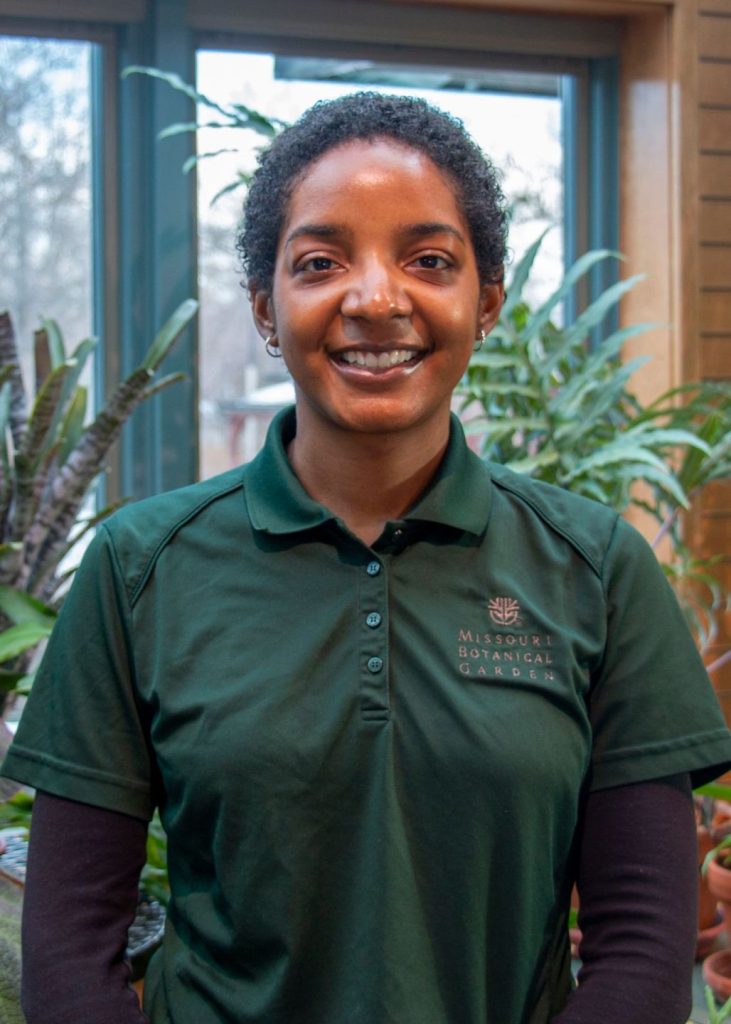 Portrait photo of Daria McKelvey from Missouri Botanical Gardens. Daria has dark complexion, short curly hair, and wearing a forest green polo shirt with a long-sleeved tshirt underneath.