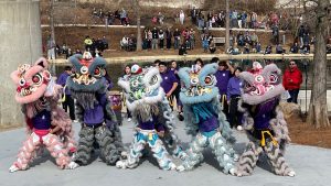 5 colorful lion dancers from the Asian District of Oklahoma City performing at Myriad Gardens while a crowd watches.